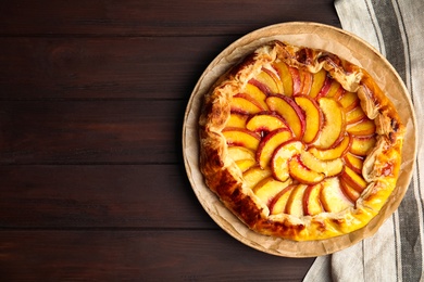 Photo of Delicious fresh peach pie on wooden table, top view. Space for text