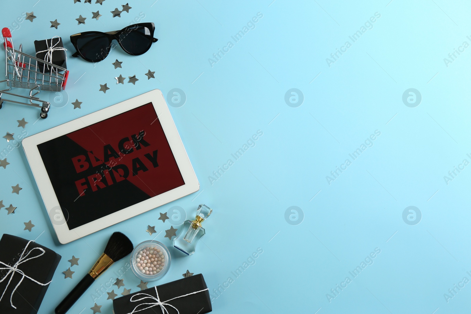 Photo of Flat lay composition with tablet, gifts and accessories on light blue background, space for text. Black Friday sale