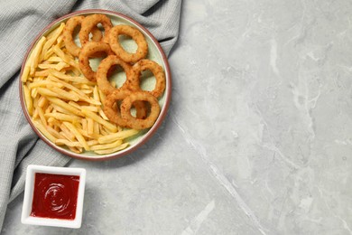 Tasty ketchup, fries and onion rings on light grey table, flat lay. Space for text