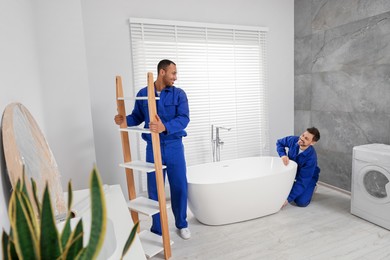 Photo of Male movers with bathtub and rack in bathroom. New house