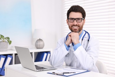 Photo of Medical consultant with glasses and stethoscope at table in clinic