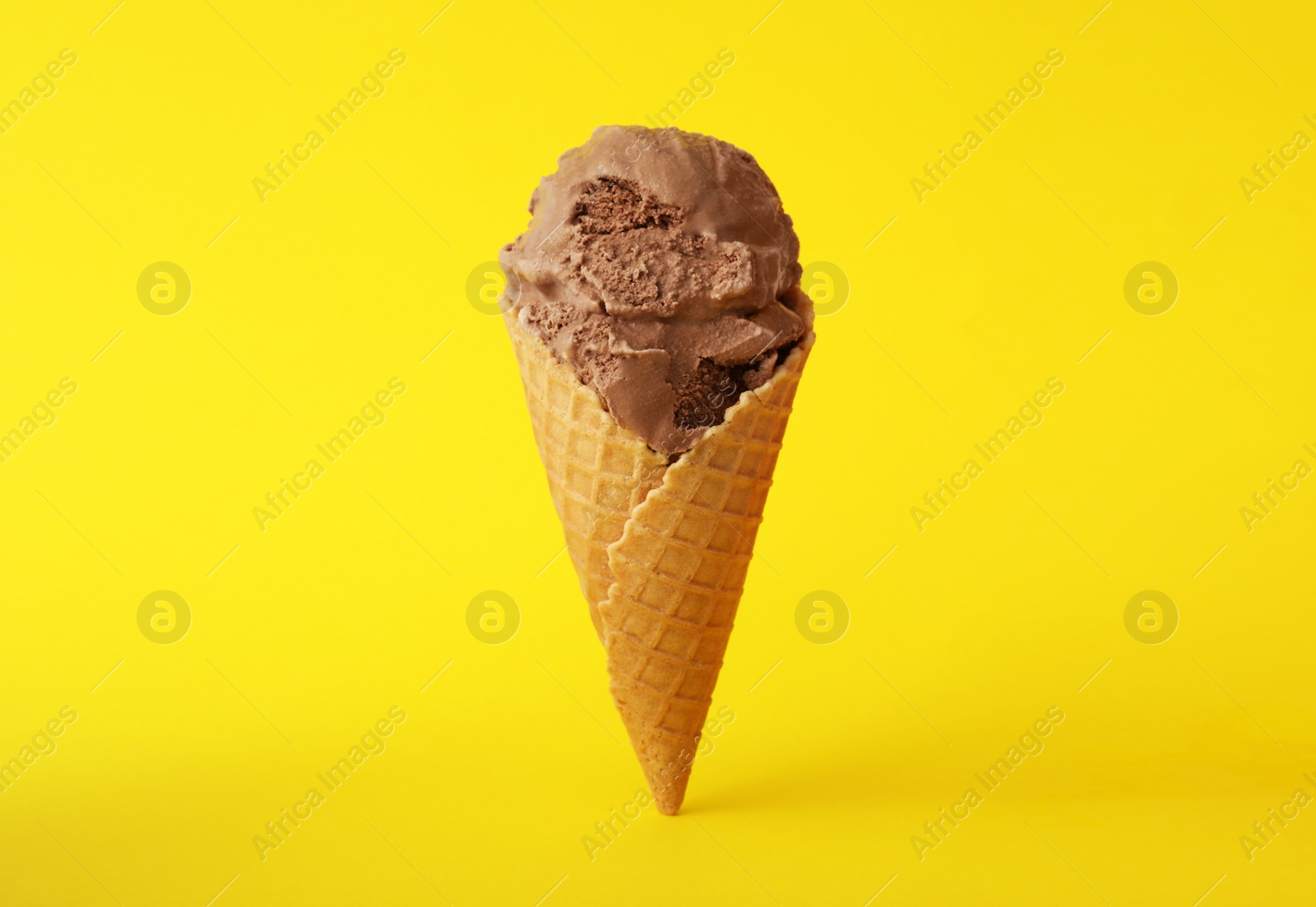 Photo of Delicious chocolate ice cream in waffle cone on yellow background