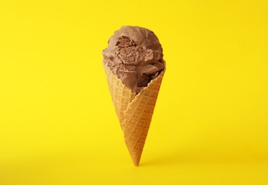 Photo of Delicious chocolate ice cream in waffle cone on yellow background