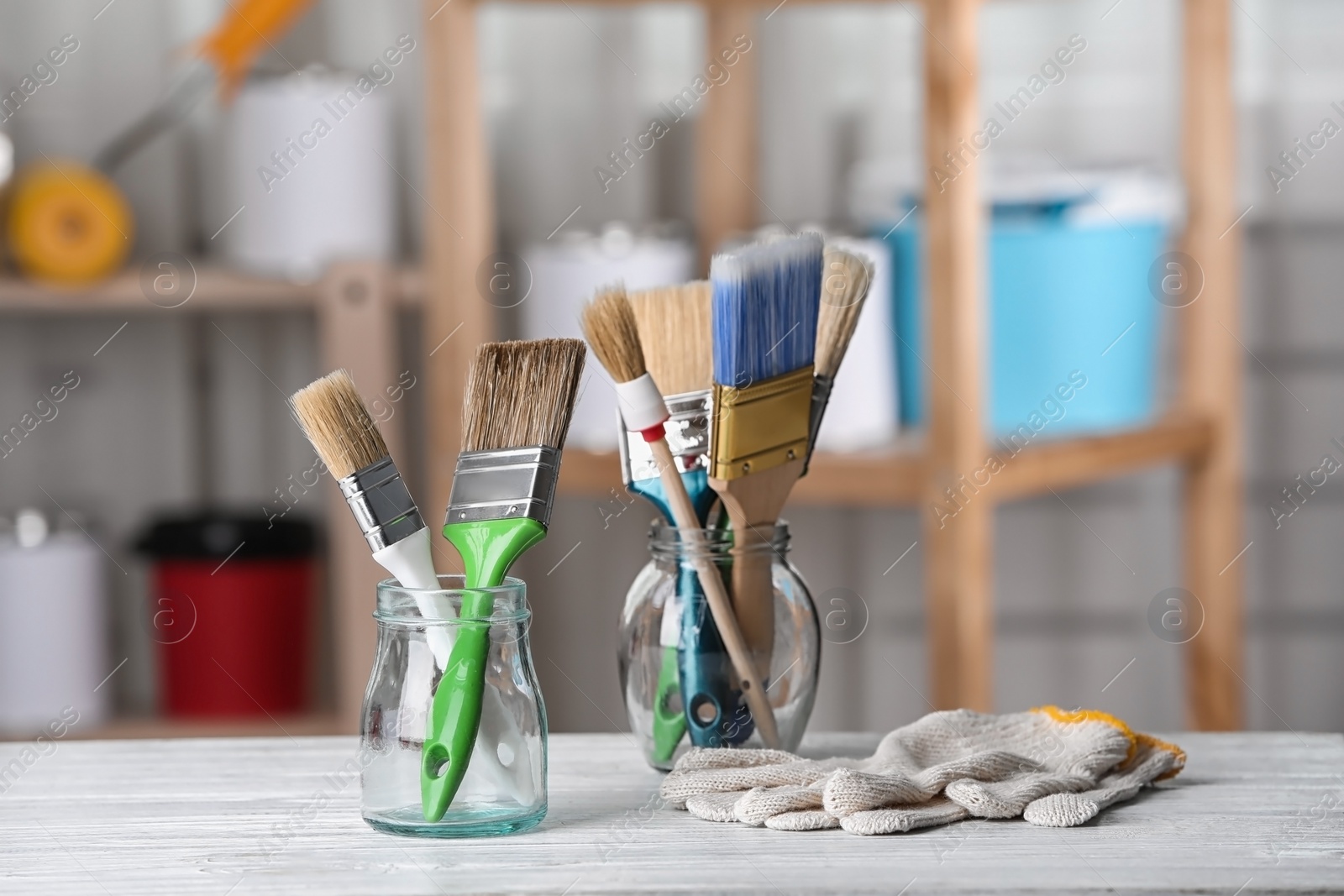 Photo of Glass jars with paint brushes and gloves on table in workshop