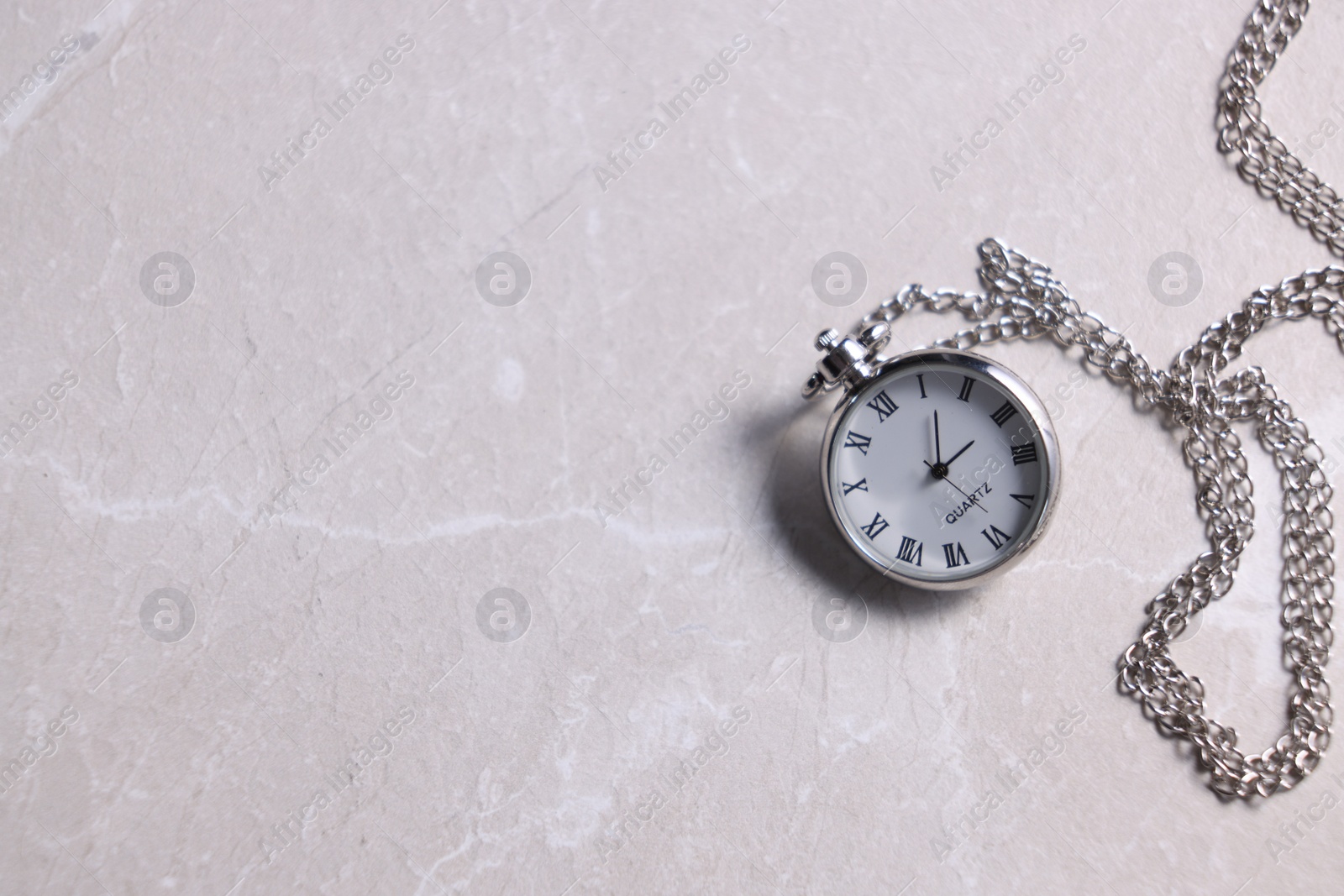 Photo of Silver pocket clock with chain on grey textured table, top view. Space for text