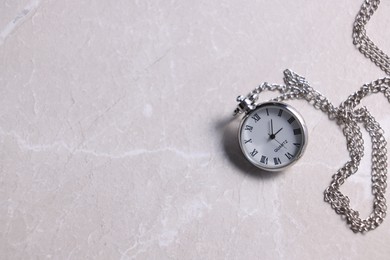 Silver pocket clock with chain on grey textured table, top view. Space for text