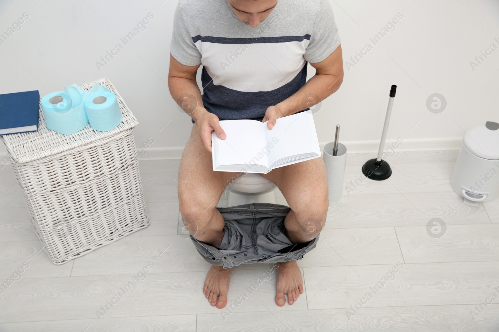 Photo of Young man with book sitting on toilet bowl in bathroom