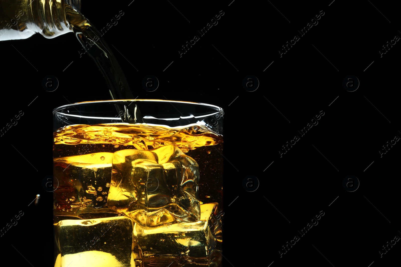 Photo of Pouring whiskey into glass with ice cubes on black background, closeup. Space for text