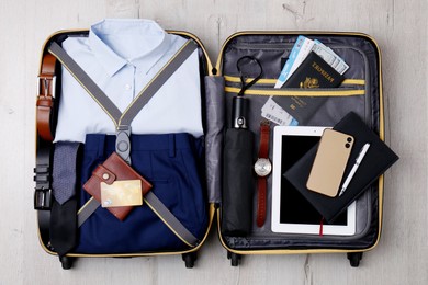 Packed suitcase with business trip stuff on wooden surface, top view
