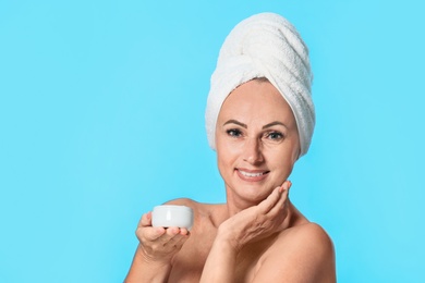 Portrait of beautiful mature woman with perfect skin holding jar of cream on light blue background