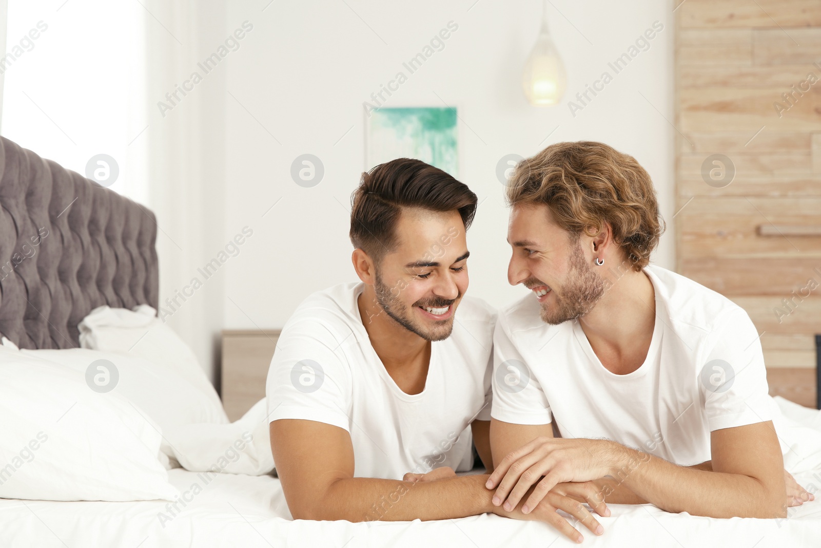 Photo of Happy gay couple lying on bed at home