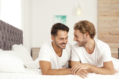 Photo of Happy gay couple lying on bed at home