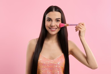 Photo of Beautiful woman applying makeup with brush on pink background