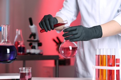 Photo of Scientist pouring reagent into flask at table in chemistry laboratory