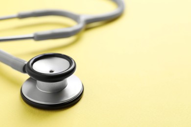 Stethoscope on yellow background, closeup. Space for text
