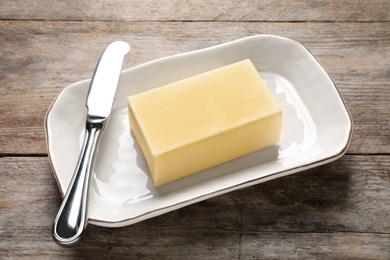 Dish with fresh butter and knife on wooden table