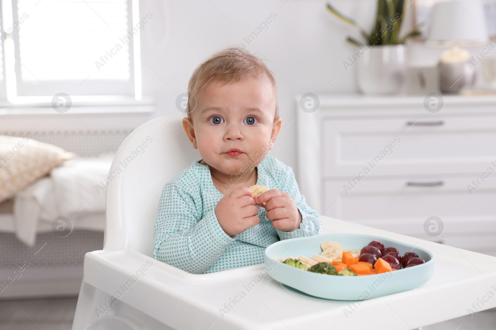 Photo of Cute little baby eating food in high chair at home