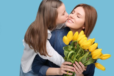 Photo of Mother and her cute daughter with bouquet of yellow tulips on light blue background