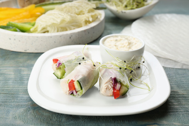 Photo of Delicious rolls wrapped in rice paper served on light blue wooden table