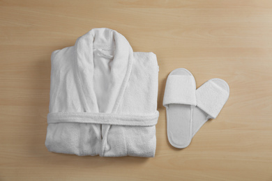 Photo of Clean folded bathrobe and slippers on wooden background, flat lay