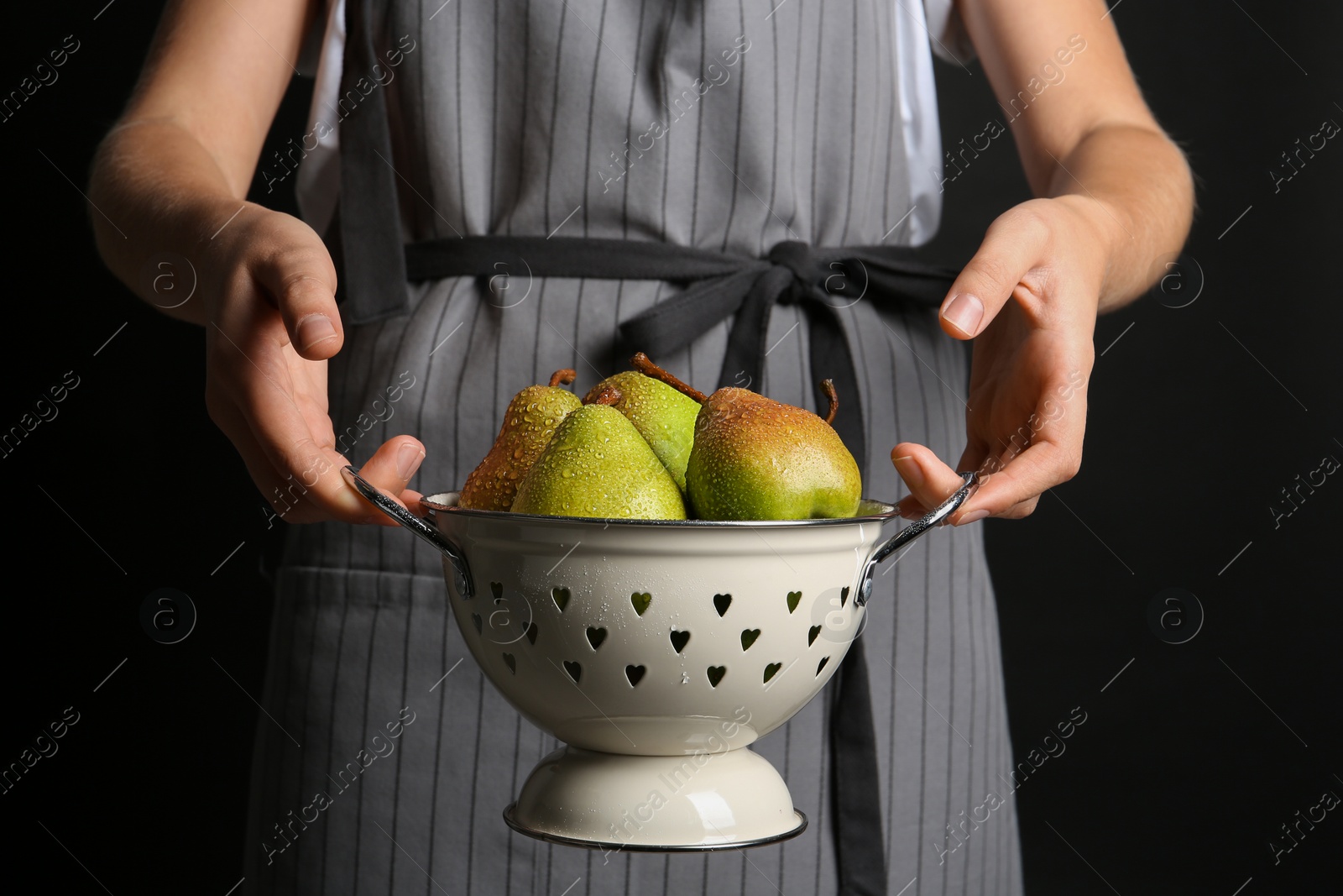 Photo of Woman holding colander with ripe pears on black background, closeup