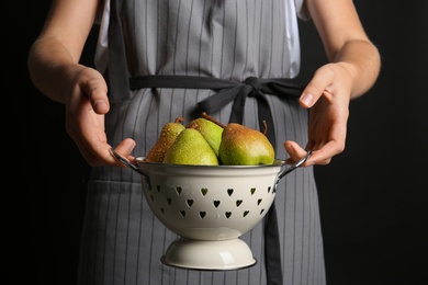 Woman holding colander with ripe pears on black background, closeup