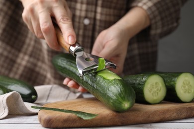 Photo of Woman peeling fresh cucumber at white wooden table, closeup