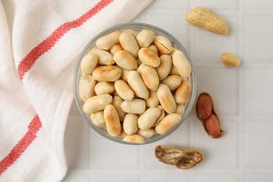 Photo of Roasted peanuts in bowl on white tiled table, top view