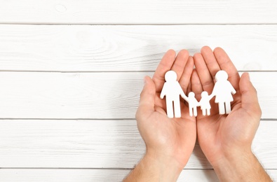 Photo of Young man holding family figure in his hands against white wooden background, top view. Space for text