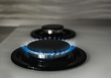 Gas burner with blue flame on modern stove, closeup