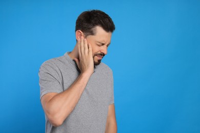 Man suffering from ear pain on light blue background, space for text