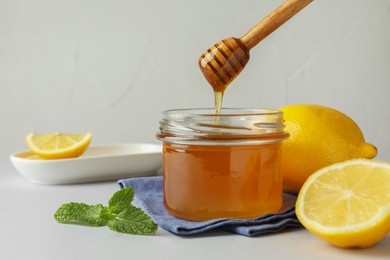 Photo of Dripping sweet honey from dipper into jar and fresh lemons on white table, space for text