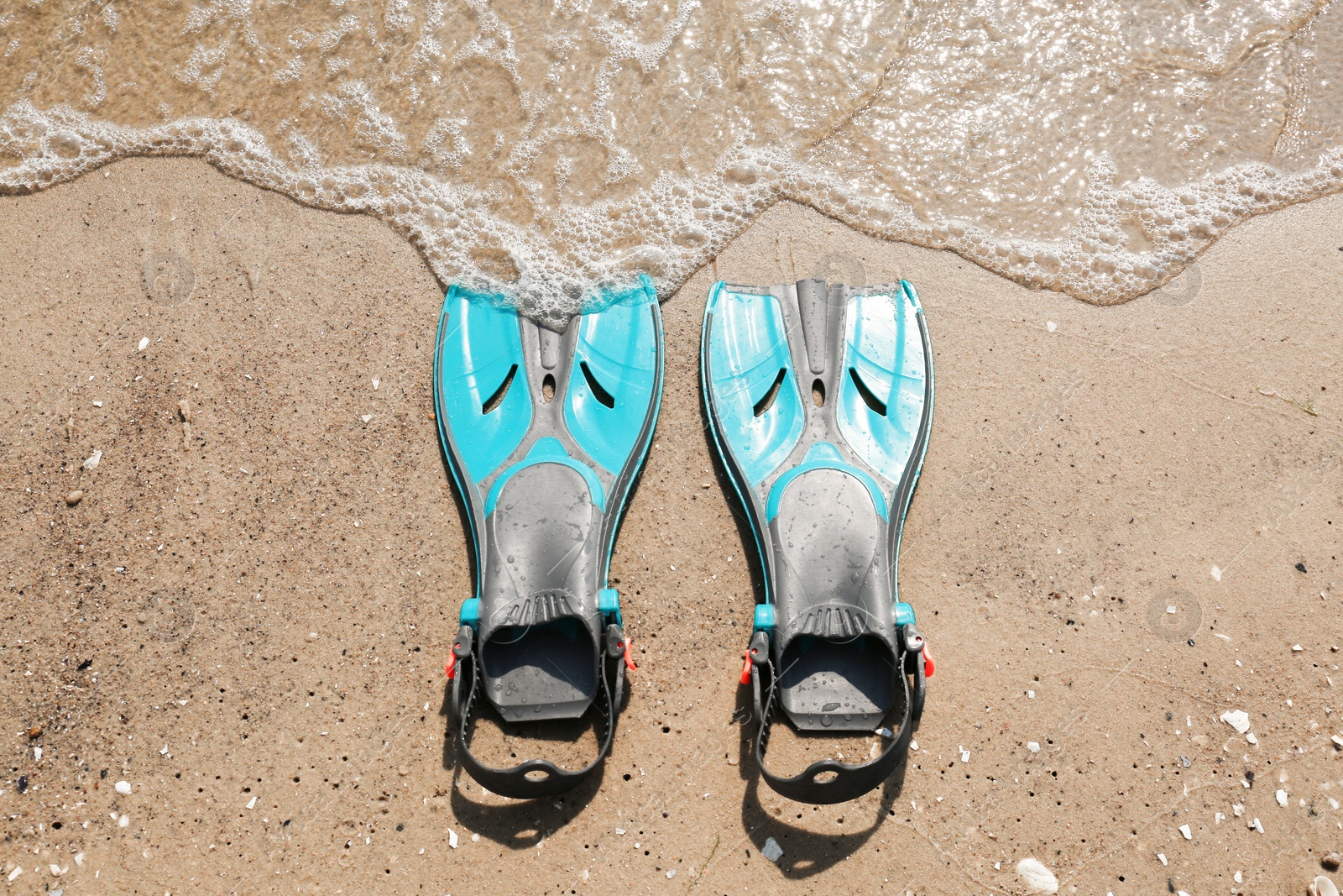 Photo of Pair of turquoise flippers on sand near sea, top view