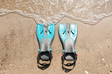 Photo of Pair of turquoise flippers on sand near sea, top view