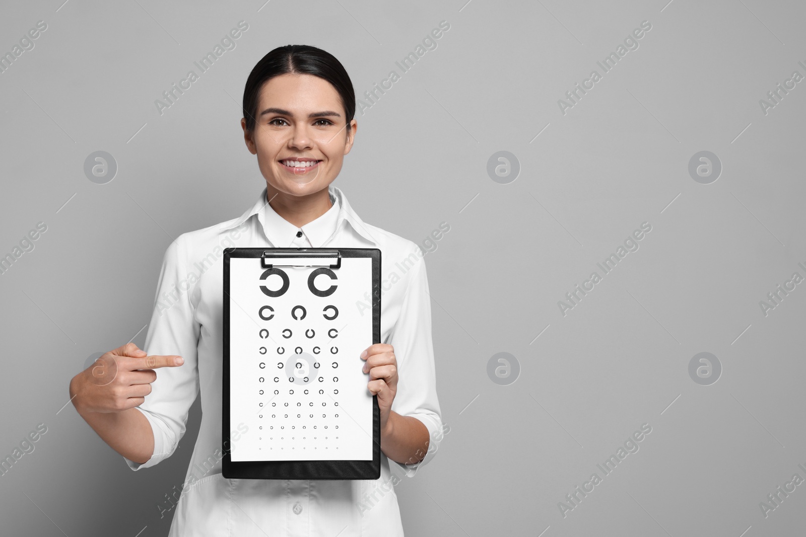 Photo of Ophthalmologist pointing at vision test chart on gray background, space for text