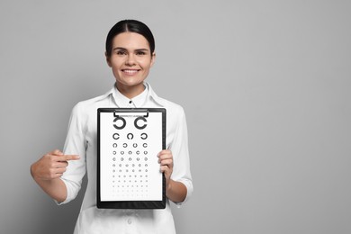 Ophthalmologist pointing at vision test chart on gray background, space for text