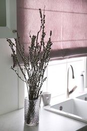 Beautiful blooming pussy willow branches in kitchen, space for text