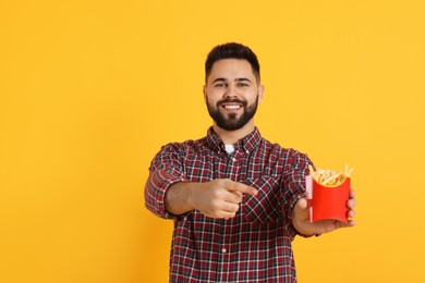 Photo of Young man with French fries on orange background, space for text