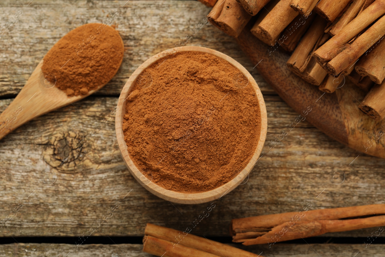 Photo of Bowl of cinnamon powder and sticks on wooden table, flat lay