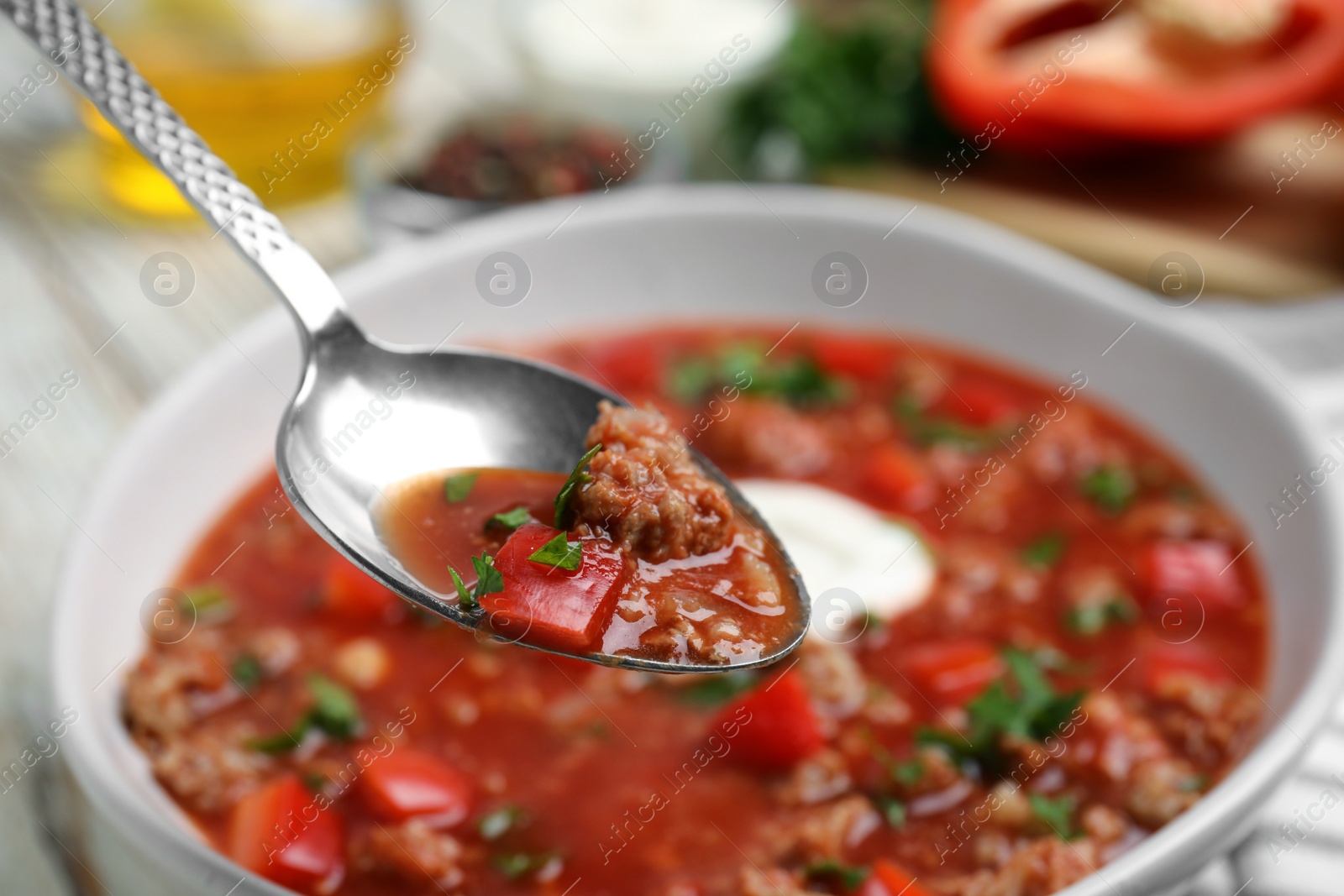 Photo of Spoon with delicious stuffed pepper soup above bowl, closeup