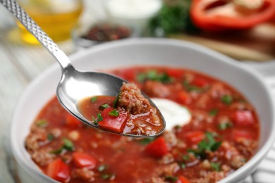 Spoon with delicious stuffed pepper soup above bowl, closeup