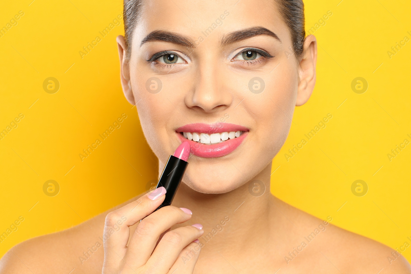 Photo of Young woman applying lipstick on color background