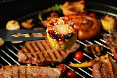 Photo of Barbecue fork with corn and grilled meat steaks on background