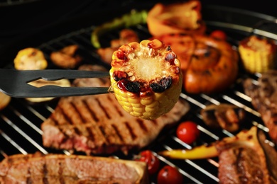 Barbecue fork with corn and grilled meat steaks on background