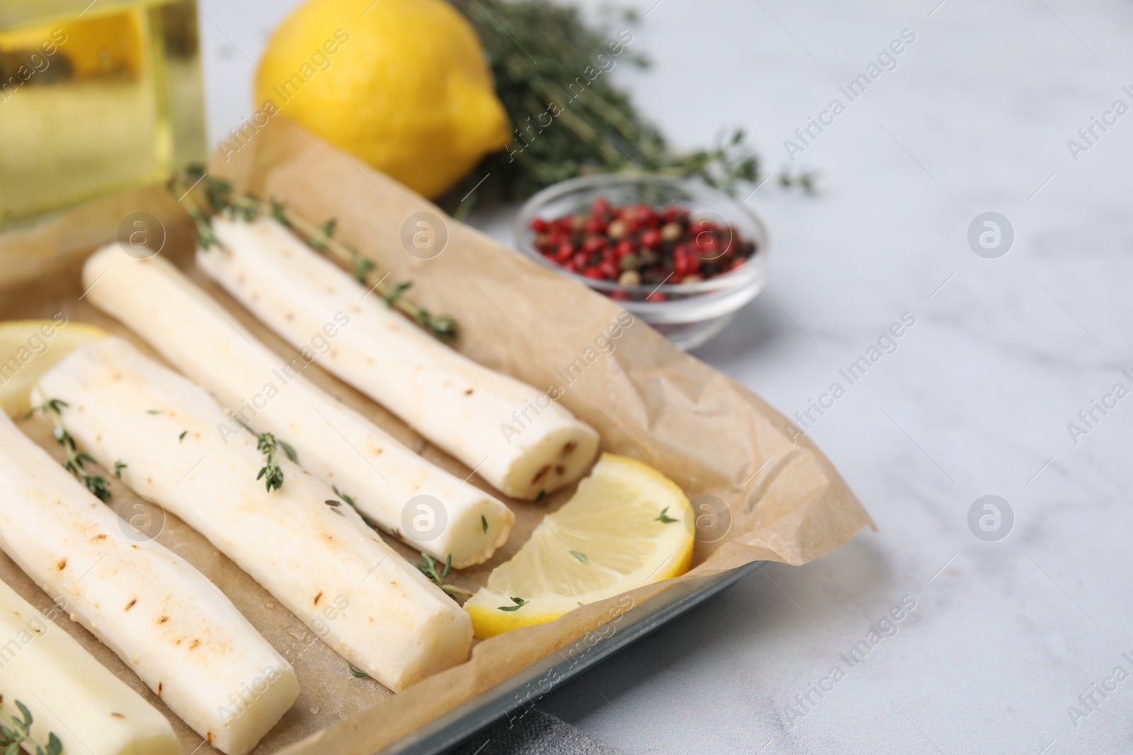 Photo of Baking tray with raw salsify roots, lemon and thyme on white marble table, closeup. Space for text