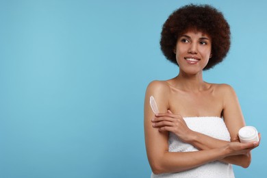 Photo of Beautiful young woman applying body cream onto arm on light blue background, space for text
