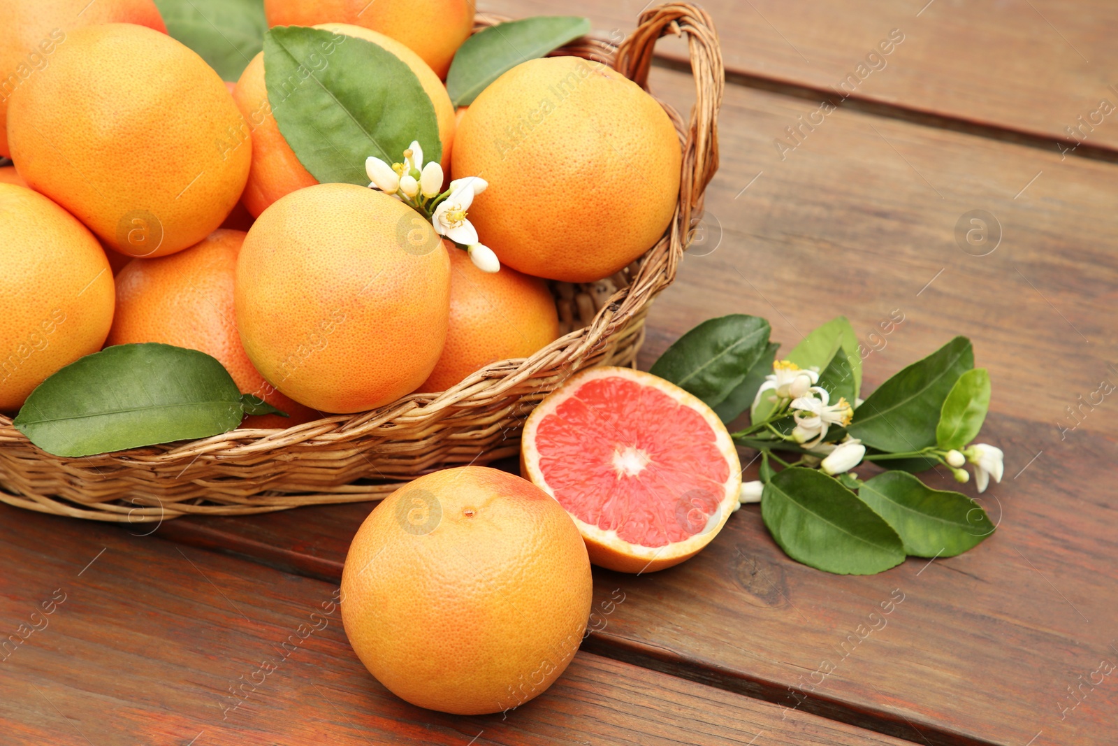Photo of Wicker basket with fresh grapefruits and green leaves on wooden table