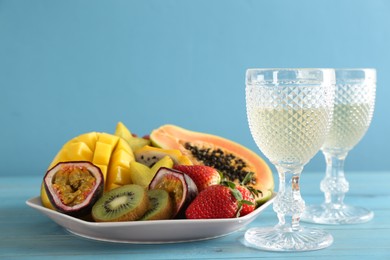 Photo of Delicious exotic fruits and glasses of wine on light blue wooden table