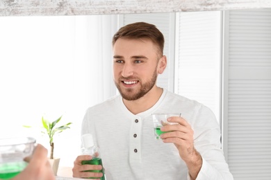 Photo of Young man with mouthwash against mirror in bathroom. Teeth and oral care