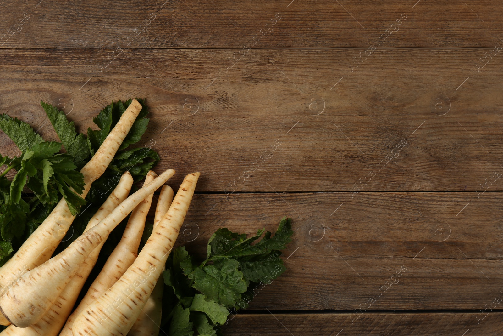 Photo of Fresh ripe parsnips with leaves on wooden table, flat lay. Space for text